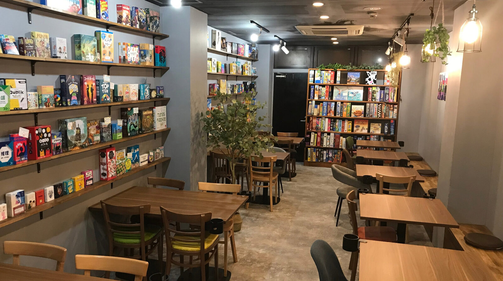 JELLY JELLY CAFE 福岡天神店の店内。壁一面の棚にボードゲームが並び、木のテーブルと椅子が置かれている。